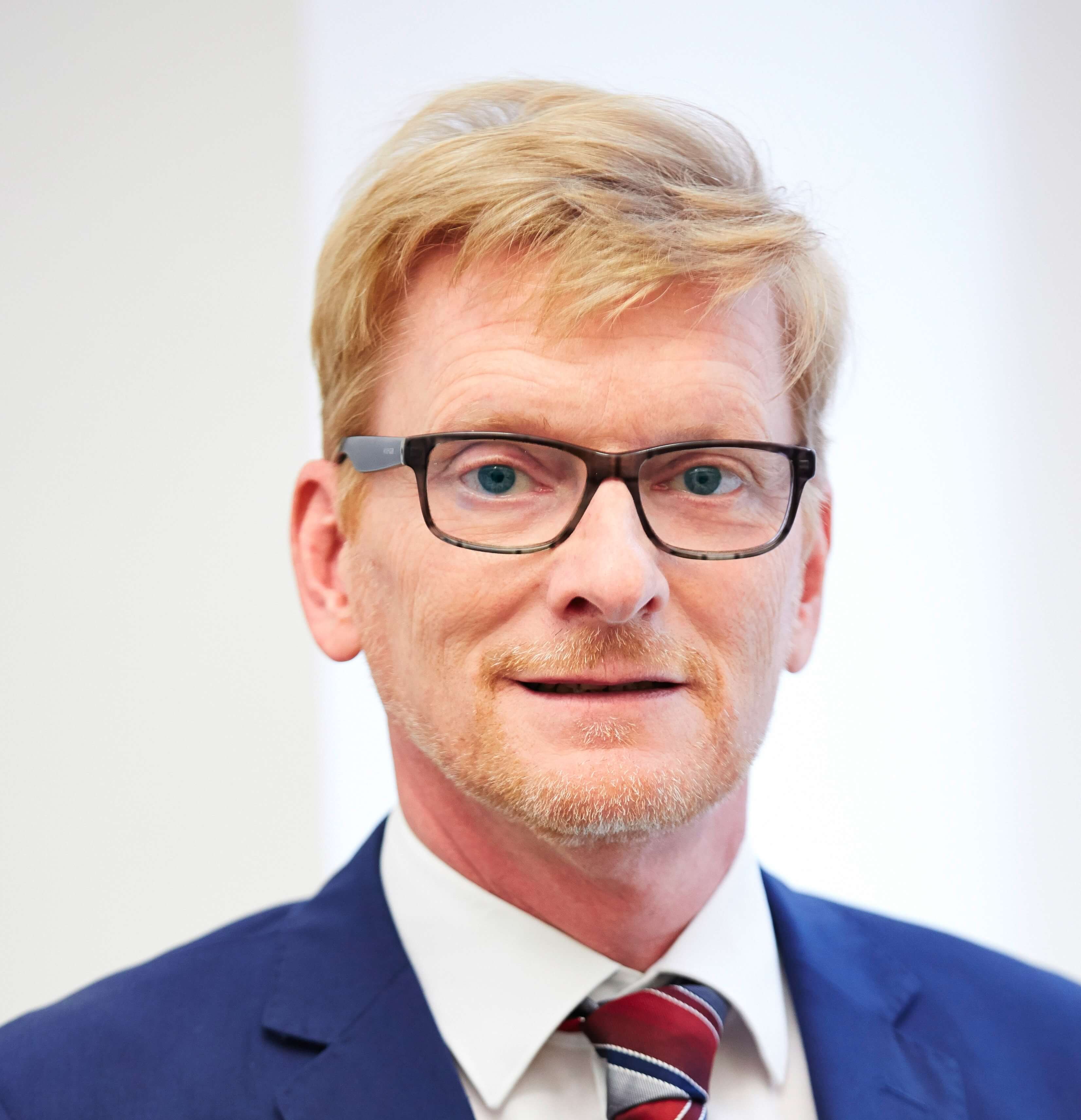Michael Holubowsky filialleiter-michael-holubowsky-in-blauem-anzug-mit-blonden-haaren-und-einer-brille