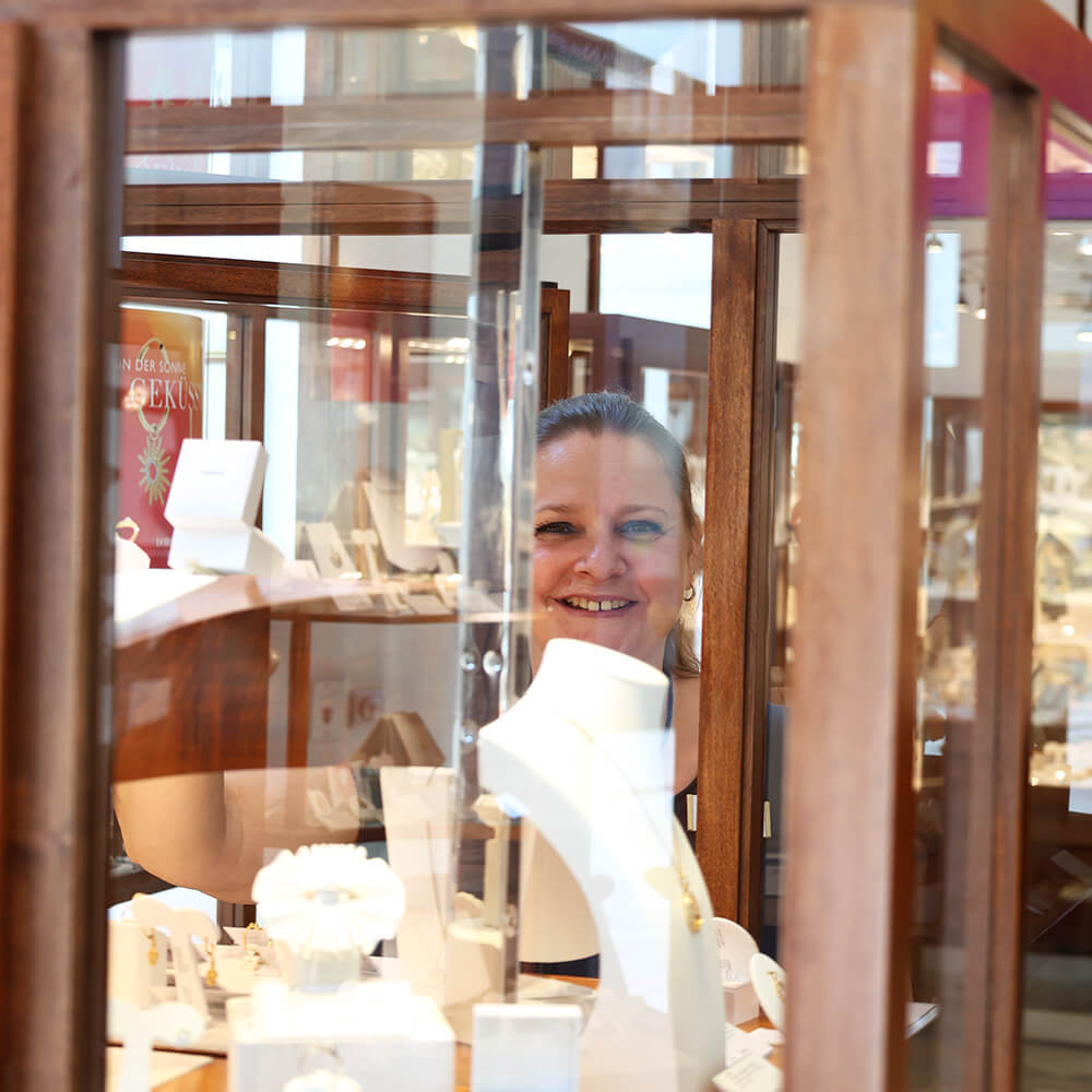 Dr. Monika Leiss filialleiterin-hinter-einer-vitrine-laechelnd-durch-das-glas