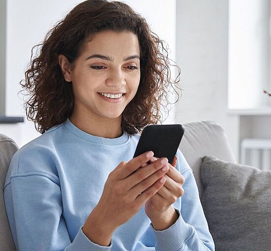 Junge Frau am Sofa mit Smartphone